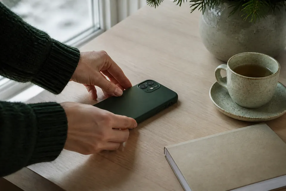 Händer som lägger en mobiltelefon med skärmen nedåt på ett träbord bredvid en kopp te